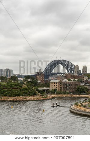 Sydney Australia - March 21 2017: Sydney Harbour bridge under gray rainy sky behind green Barangaroo Reserve and Munns Slipway. Barangaroo skyline and bay water in front.