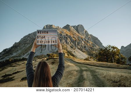 Tablet With Text Never Stop Exploring In Woman Hands Against The Background Of The Mountain. Travel
