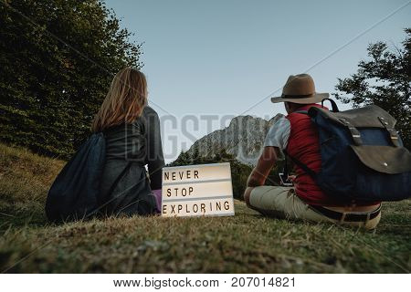 Box with text never stop exploring near man and woman backs against the background of the mountain. Travel concept