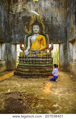 Kanchanaburi Thailand - April 13 2014: Buddhist tourist woman worshiping old Buddha image in ruined buddhist church in Kanchanaburi Thailand
