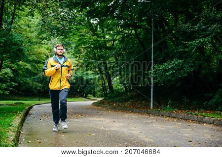 man runnin in autumn park with music in rainy weather