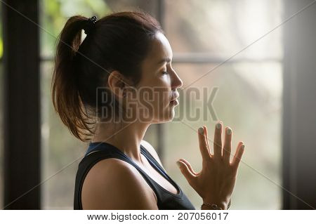 Profile portrait of young attractive woman making namaste gesture, practicing yoga at home, meditating exercise, relaxation pose, working out with eyes closed, indoor close up, studio background