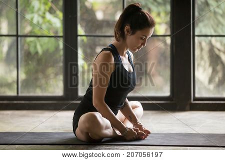 Young attractive woman practicing yoga at home, sitting in Butterfly exercise, baddha konasana pose, working out, wearing sportswear, black shorts and top, indoor full length, studio background