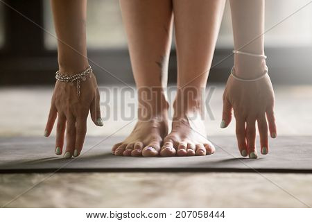 Close up of female hands touching mat, woman practicing yoga at home concept, uttanasana, head to knees, standing forward bend pose, wearing wrist bracelets, indoor close up image, floor background