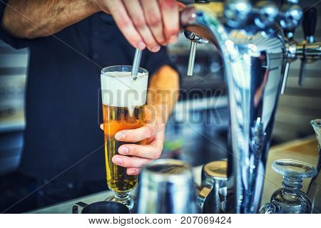 Close-up of young bartender pouring beer while standing at the bar counter.