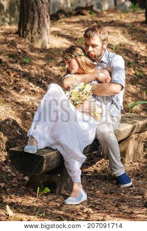 Eclectic wedding couple sitting and hugging on the bench. Rustic and hippie style pair