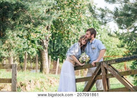 Eclectic wedding  couple outdoor. Bride and groom stand near rustic gate on the farm