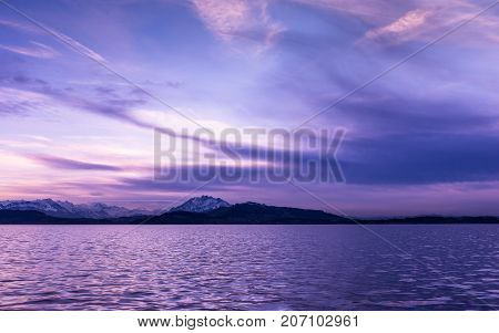 Luxury sunset in lilac over lake Zug. Switzerland. In the background silhouettes of the top of mountains in snow.