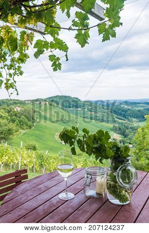Glass white wine and jars with grapes and candle on wooden barrel near vineyard on south Styrian wine route in Austria