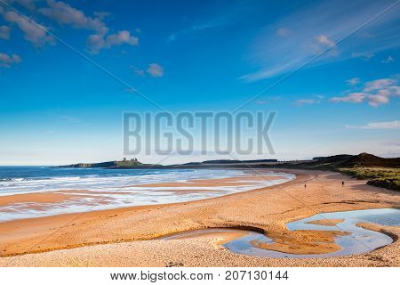 Embleton Burn snakes across Embleton Beach, which is a wide sandy bay, with the ruins of Dunstanburgh Castle providing a stunning backdrop located on the Northumberland coastline with Embleton Burn in the foreground