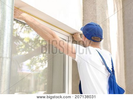 Man measuring window prior to installation of roller shutter outdoors