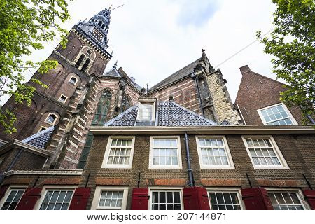 Lateral picture of the Old Church (Oude Kerk) facade with trees in a cloudy day. Amsterdam Netherlands.