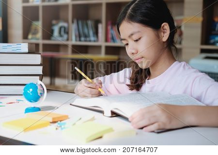 Girl Reading And Writing In Library Of School.