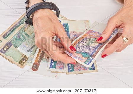 Female manicured hands holding kyat money. Close up woman hands holding money of Myanmar kyat, Burma banknotes, white wooden background.