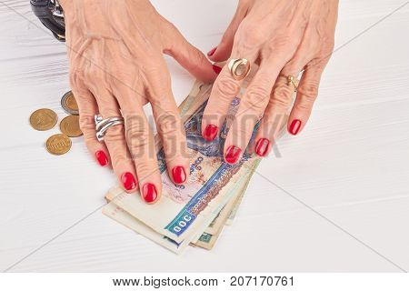 Red manicure and Burma banknotes. Senior woman well-groomed hands and kyat money, white wooden background.