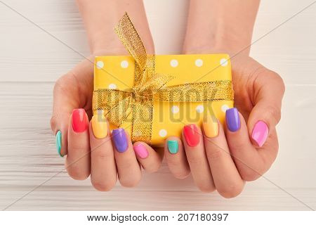 Little gift box in female manicured hands. Woman hands with pastel nail polish holding yellow dotted box with gift.