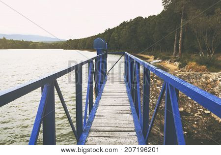 Mole  on the scandinavian lake with motorboat on side and misty hills. Blue wooden bridge in forest in autumn time with blue lake. Lake for fishing with pier and powerboat. Foggy lake with hills