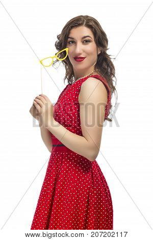 Portrait of Alluring Caucasian Female Holding Yellow Artistic Spectacles In Front. Posing In Red Polka Dot Dress Against Pure White.Vertical Shot