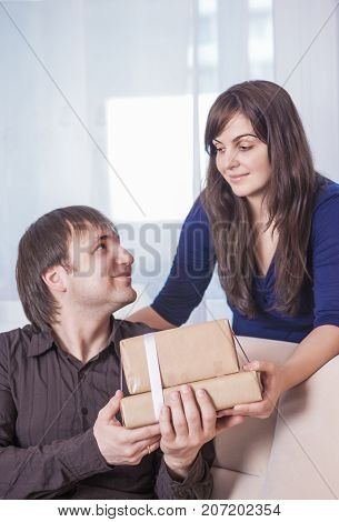 Relationships Ideas and Concepts. Portrait of Caucasian Brunette Wife Giving a Present to Her Husband. Vertical Image Composition
