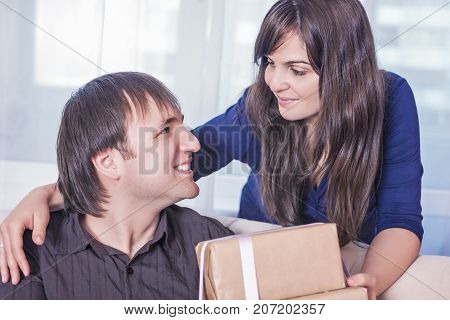 Relationships Ideas and Concepts. Portrait of Caucasian Brunette Wife Giving a Present to Her Husband. Horizontal Shot