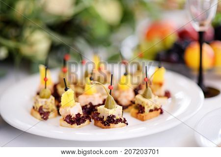 Delicious canape snacks with pineapple and capers topping served on a party or wedding reception. Plates with assorted appetizers on an event party or dinner.
