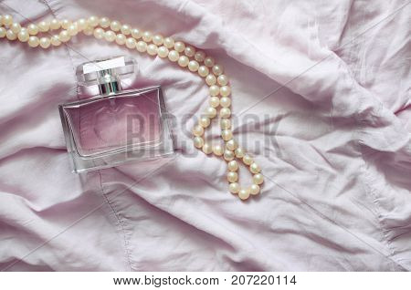 Women's perfume and pearl beads on a pink delicate fabric. Toning.