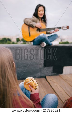 Music junkie with junk food on live show. Girl with fastfood in hands listen singer's acoustic guitar improvisation.