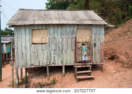 Boca de valeria Brazil - December 03 2015: hut on piles and boy child in village on mud background. Poverty and childhood concept.