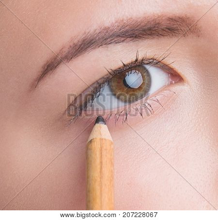 Beautiful young girl applying make up on eyes. Isolated on grey