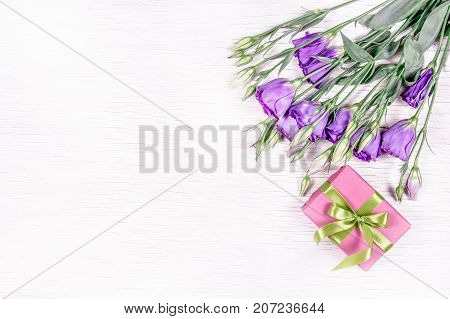 Gift with ribbon and purple flowers on a white background. A bouquet of eustoma. Copy space