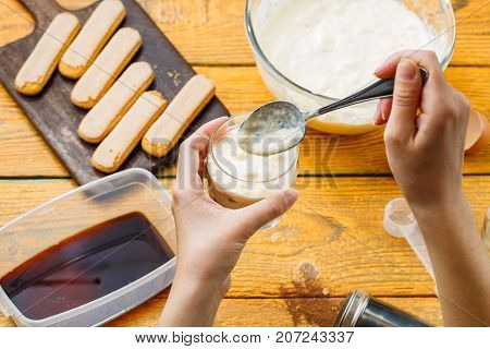 Picture on top of wooden table with savoyardi biscuits, coffee, cream cheese, human hands