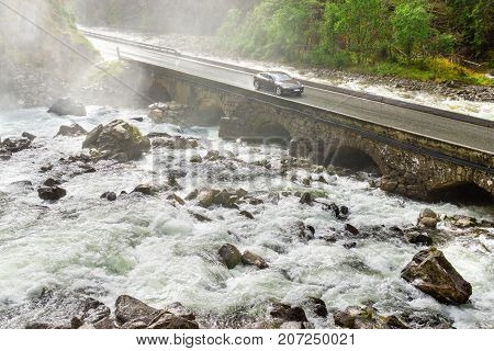 Electric car drives on bridge crossing river. Renewable energy from hydropower used for zero emission vehicle. Climate protection concept. Latefoss, Norway.