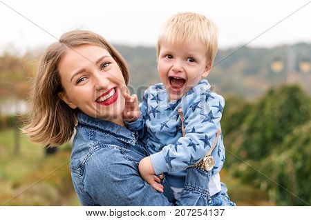 Happy joyful mother having fun throws up in the air child in autumn park