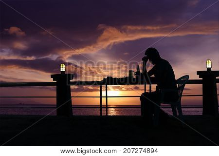 Silhouette sad man drinking beer at the beach with red sky sunset background. Asian troubled guy with bottle of alcohol