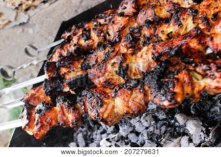 closeup of some meat skewers being grilled in a barbecue. side view