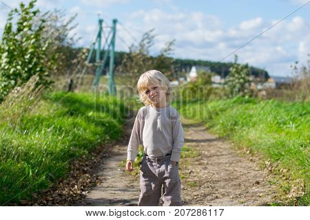 Seriouse blond boy staying embraced himself with his arms, country road to the Urals village