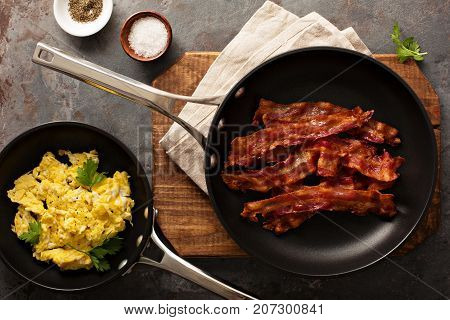 Cooked sizzling hot tasty crispy bacon on a skillet and scrambled eggs ready for breakfast overhead shot