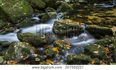Waterfall falling on stones through autumn forest. Fall nature specification. Stones along and in the river in forest.