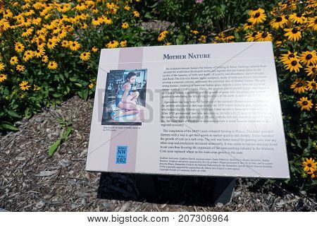 JOLIET, ILLINOIS / UNITED STATES - JULY 25, 2017: A plaque, in the flower garden below the "Mother Nature" sculpture in the Route 66 Park, describes the significance of the statue.