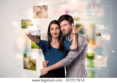 Collecting memories concept with photos in backbround and a happy young couple in love taking selfie with a mobile phone