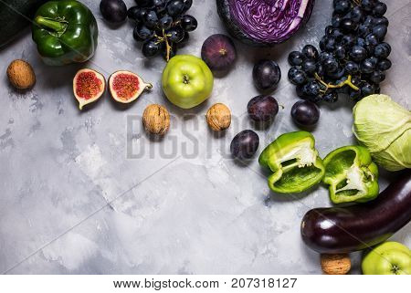 Fresh organic raw green and purple colored vegetables and fruits on stone background. Top view. Copyspace