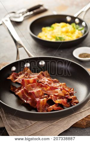 Cooked sizzling hot tasty crispy bacon on a skillet and scrambled eggs ready for breakfast