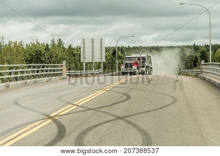 Giant red dump truck makes it way down to the trans canada on road with tire markings