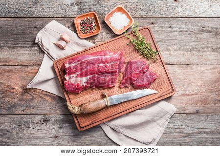 Raw roastbeef meat cut with hyme and garlic and knife on cutting board over old  wooden background, top view