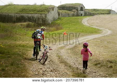Girl running for catch her father who left behind she alone. Family cyclo holidays around town of Palmanova and its defense walls and trenches, Friuli Venezia Giulia region of Italy.