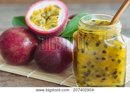 Homemade delicious passion fruit jam in bottle put on wood table. Fresh passion fruit and homemade jam on wood table in natural tone style concept. Close up bottle of passion fruit jam macro concept. Passion fruit jam ready to served.