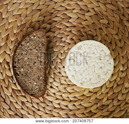 White flat round rice cracker and a piece of rye bread on whicker place mat background.