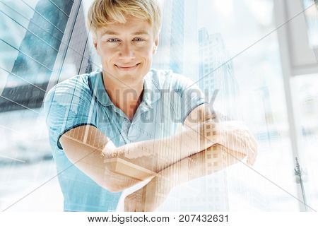 Falling in love. Close up of cute cheerful man expressing charm while standing in front of you and keeping hands together