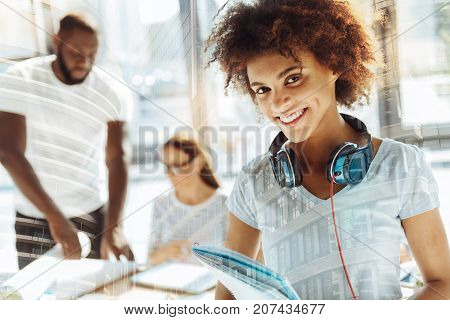 Studying again. Close up of positive smiling student expressing excitement and holding notes while her groupmates having discussion