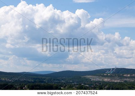 Clouds over the countryside with hills woods and ski jumps.